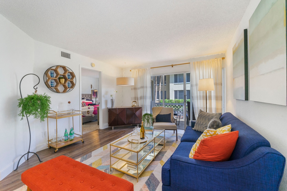 Living room with patterned area rug and colorful couch, chair, and ottoman, coffee table, and balcony door